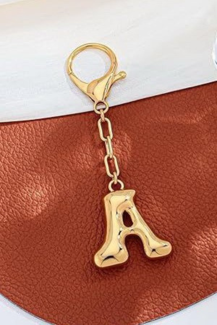 Gold letter 'A' keychain on a brown leather surface