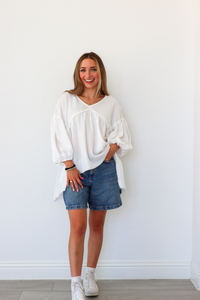 Woman wearing a white blouse and denim shorts against a white wall