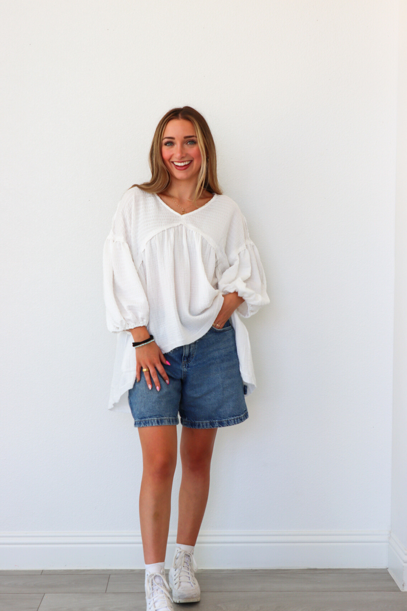 Woman wearing a white blouse and denim shorts against a white wall