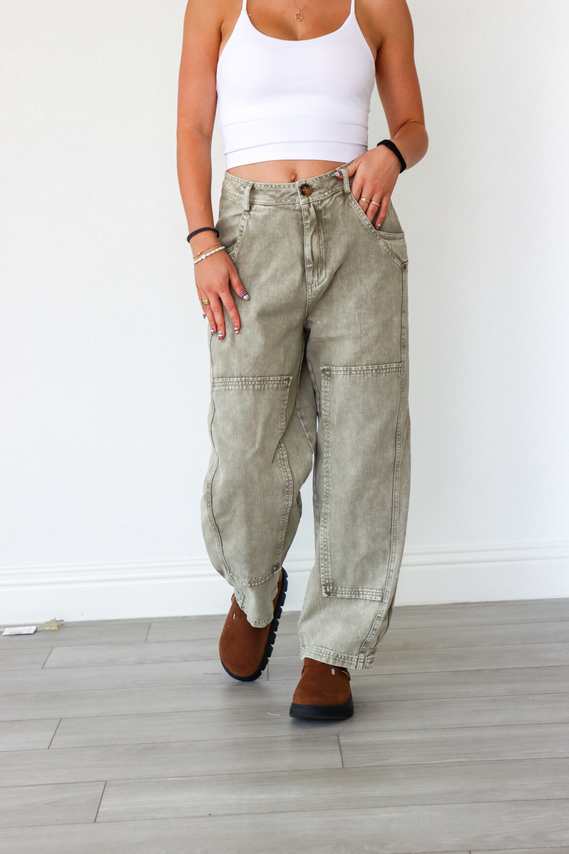 Person wearing light-colored cargo pants and a white tank top against a white wall.