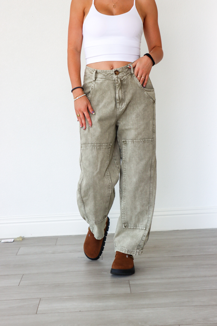 Person wearing light-colored cargo pants and a white tank top against a white wall.