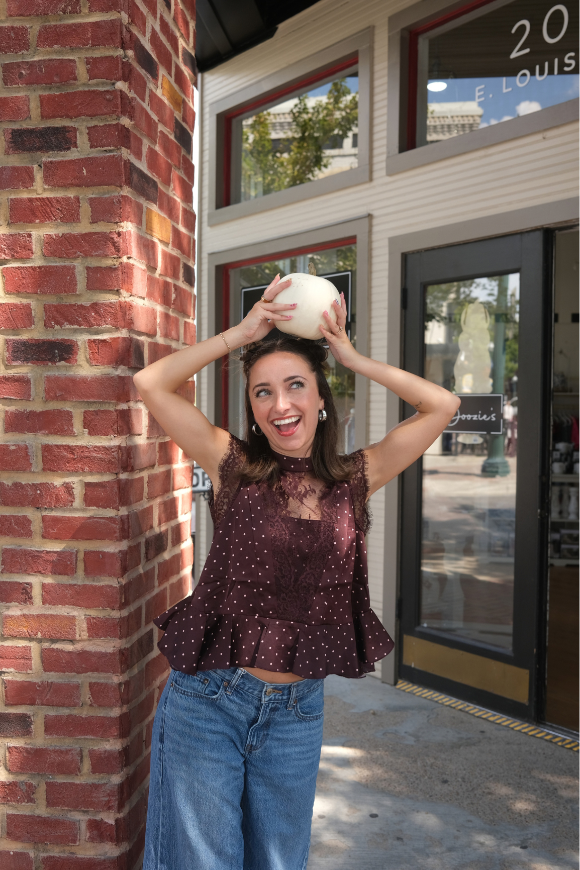 A woman wearing a sleeveless burgundy top with white polka dots and lace detailing, paired with blue jeans