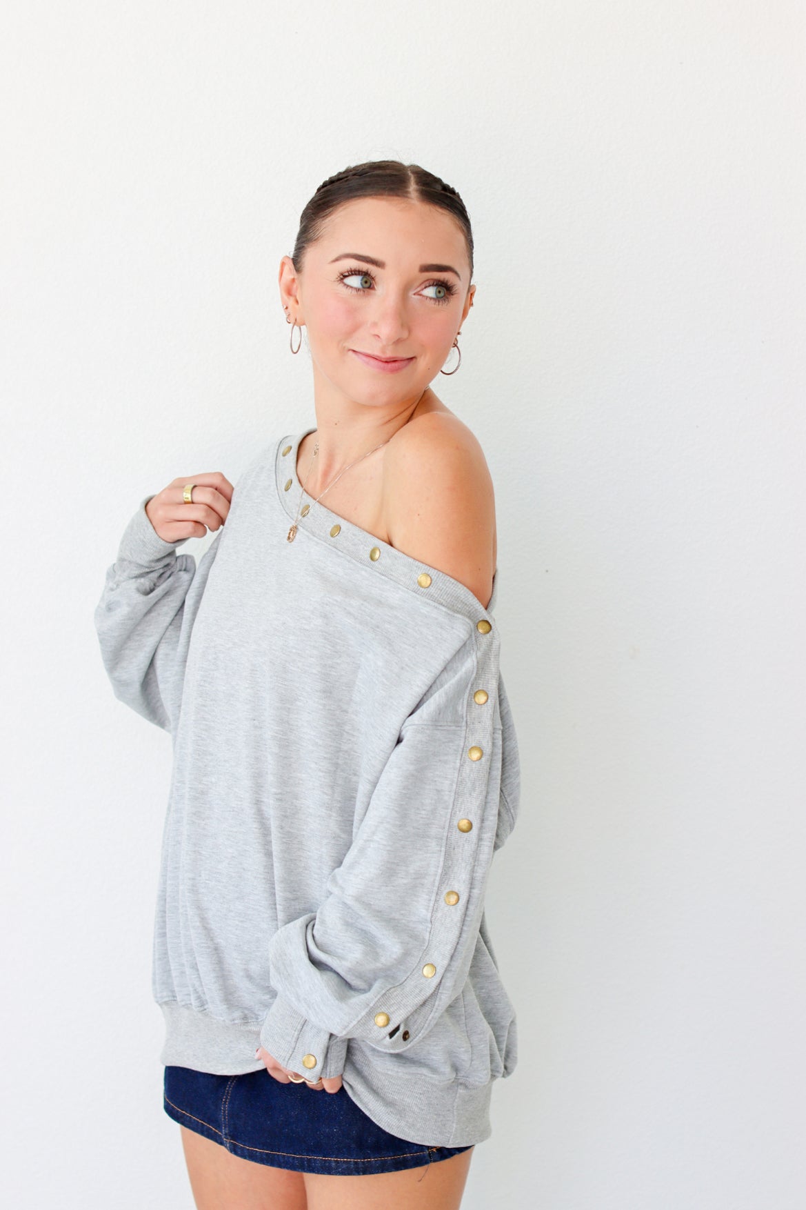 Woman wearing a light gray off the shoulder sweater with buttons along the trim 