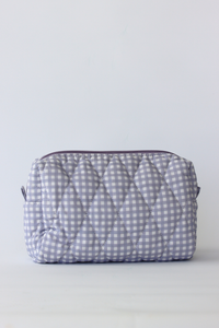 A quilted cosmetic pouch with a light blue and white gingham pattern, featuring a diamond-quilted texture and a dark purple zipper, set against a plain light gray background.