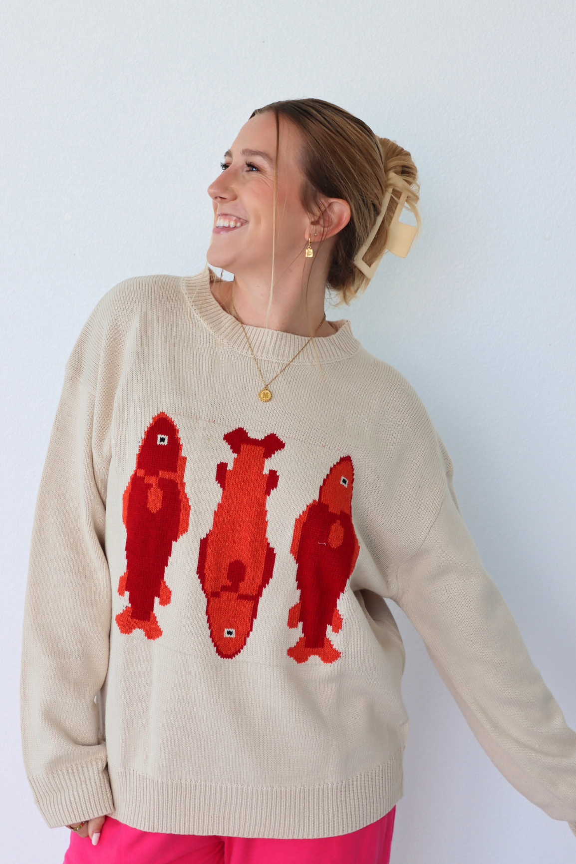Woman wearing a beige sweater with red fish patterns against a white background