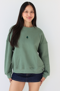 Woman wearing a green crewneck sweater with a embroidered tree in the center