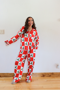 Woman wearing a red and white checkered pajama set with holiday patterns on a wooden floor.
