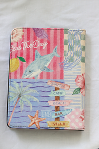 A kindle case featuring a colorful beach-themed collage with a shark, palm tree, starfish, flowers, striped background, and directional signs reading South Camp Beach and Land Bar Villa.