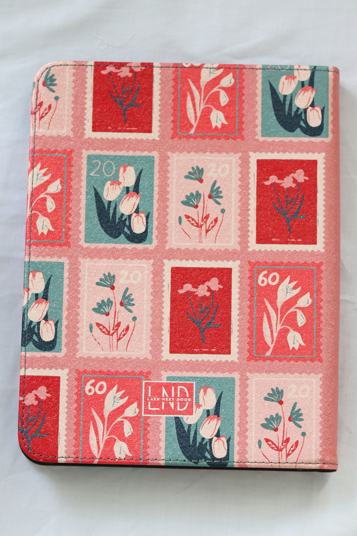 A nook case featuring a vintage-style postage stamp pattern with red, pink, and teal floral designs, photographed on a light fabric background.
