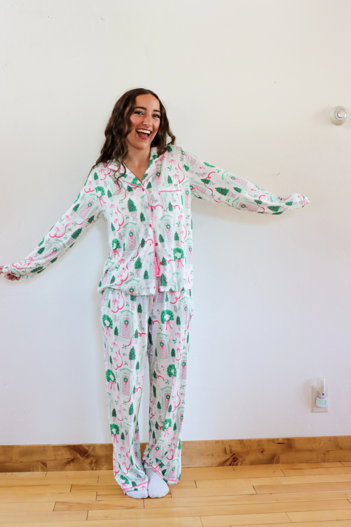 Woman wearing a floral pajama set in a room with a white wall and wooden floor.