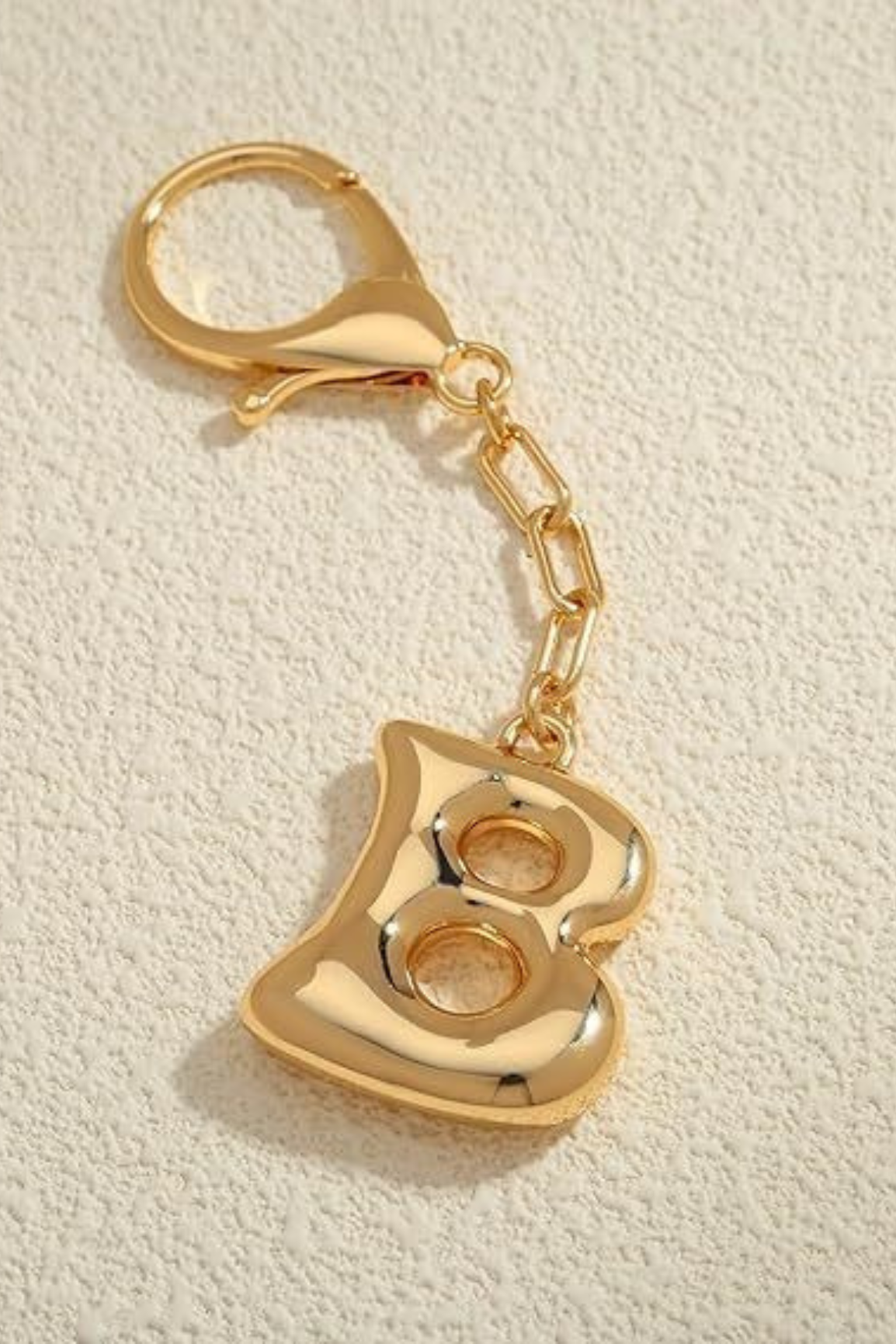 Gold keychain with letter 'B' on a beige textured background