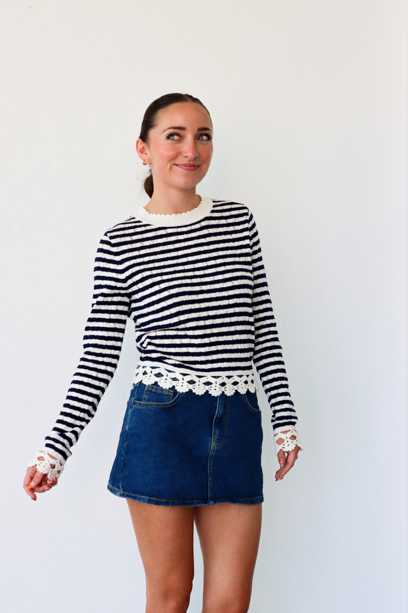 Woman wearing a black and white striped sweater with lace trim and a denim skirt on a white background