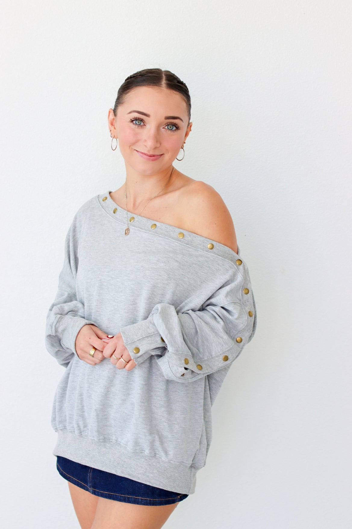 Woman wearing a light gray off the shoulder sweater with buttons along the trim 
