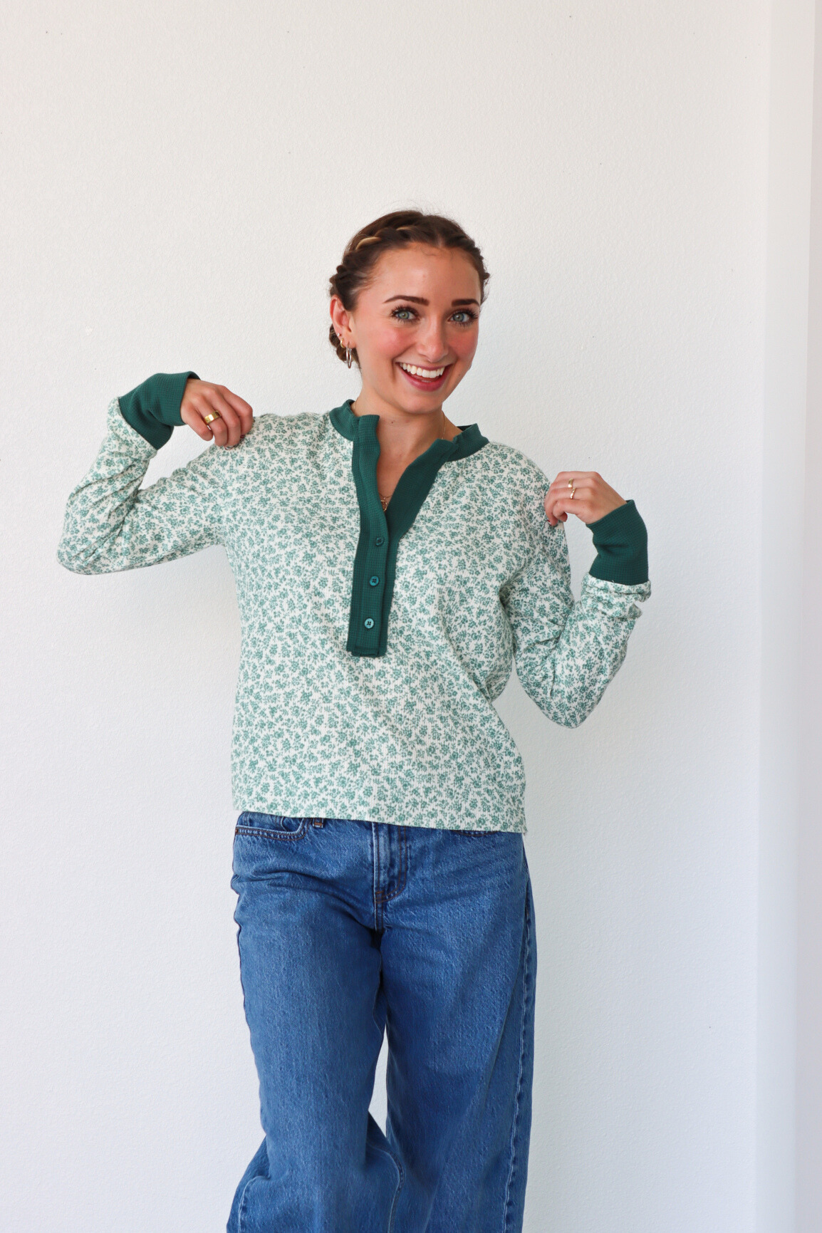 Woman wearing a green patterned shirt and blue jeans against a white background