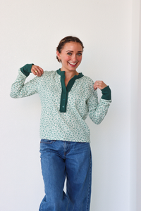 Woman wearing a green patterned shirt and blue jeans against a white background