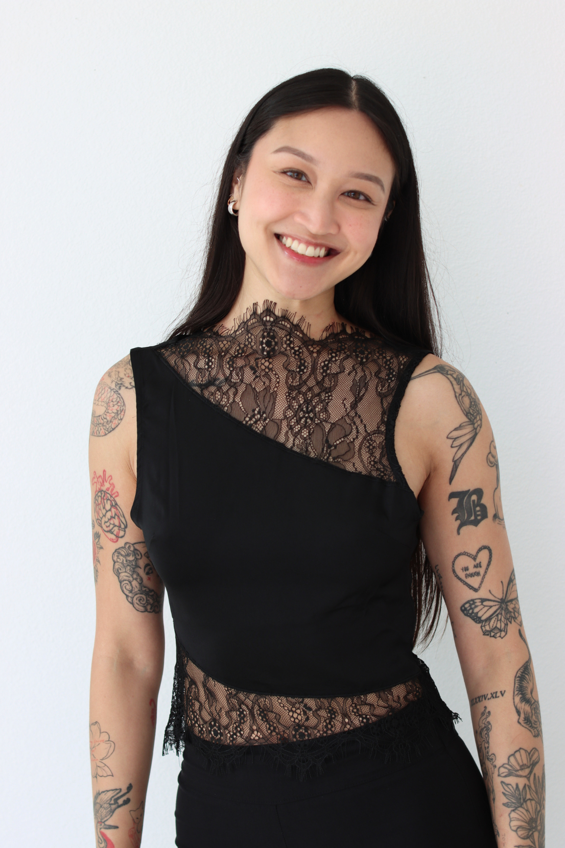 Woman wearing a black lace top with tattoos on arms against a white background
