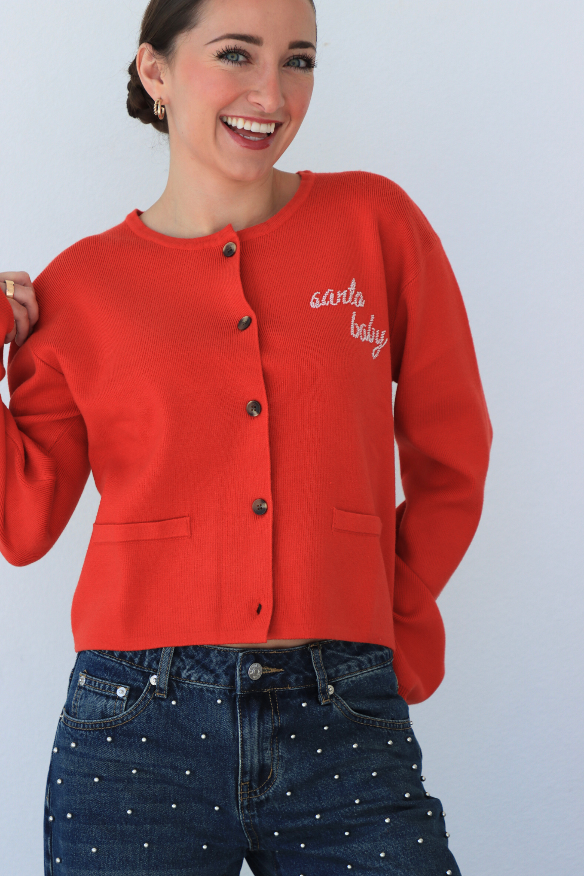 Woman wearing a red cardigan with text and blue jeans against a light gray background
