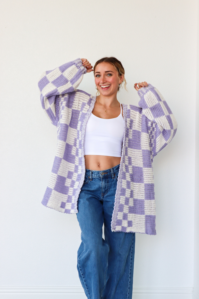 Woman wearing a purple and white checkered cardigan over a white top and blue jeans against a white background