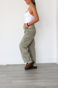 Woman wearing a white top and beige pants standing on a wooden floor.