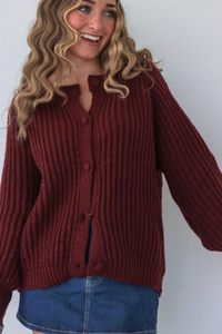 Person wearing a maroon ribbed sweater and blue jeans against a white background