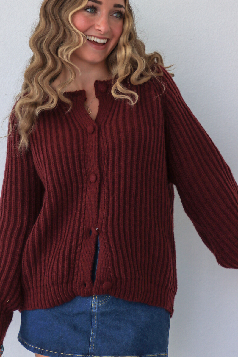 Person wearing a maroon ribbed sweater and blue jeans against a white background