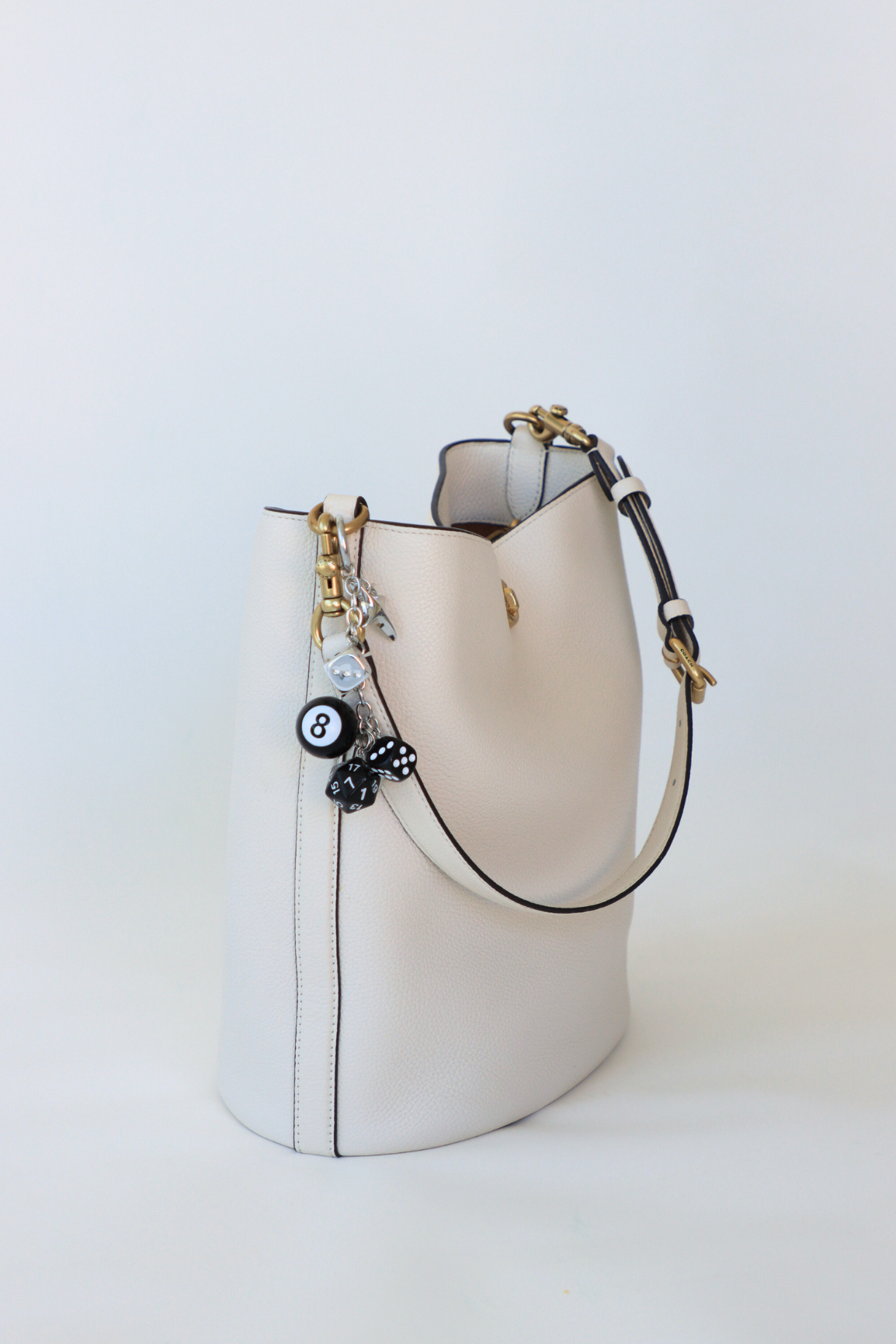 White handbag with black accents and decorative charms on a light gray background