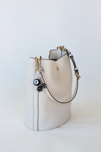 White handbag with black accents and decorative charms on a light gray background