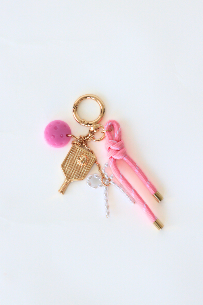 Keychain with pink pen, pom-pom, and gold key charm on a white background