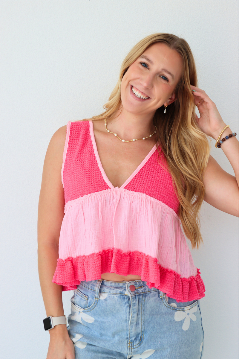 Woman wearing a pink layered top and denim shorts on a light gray background