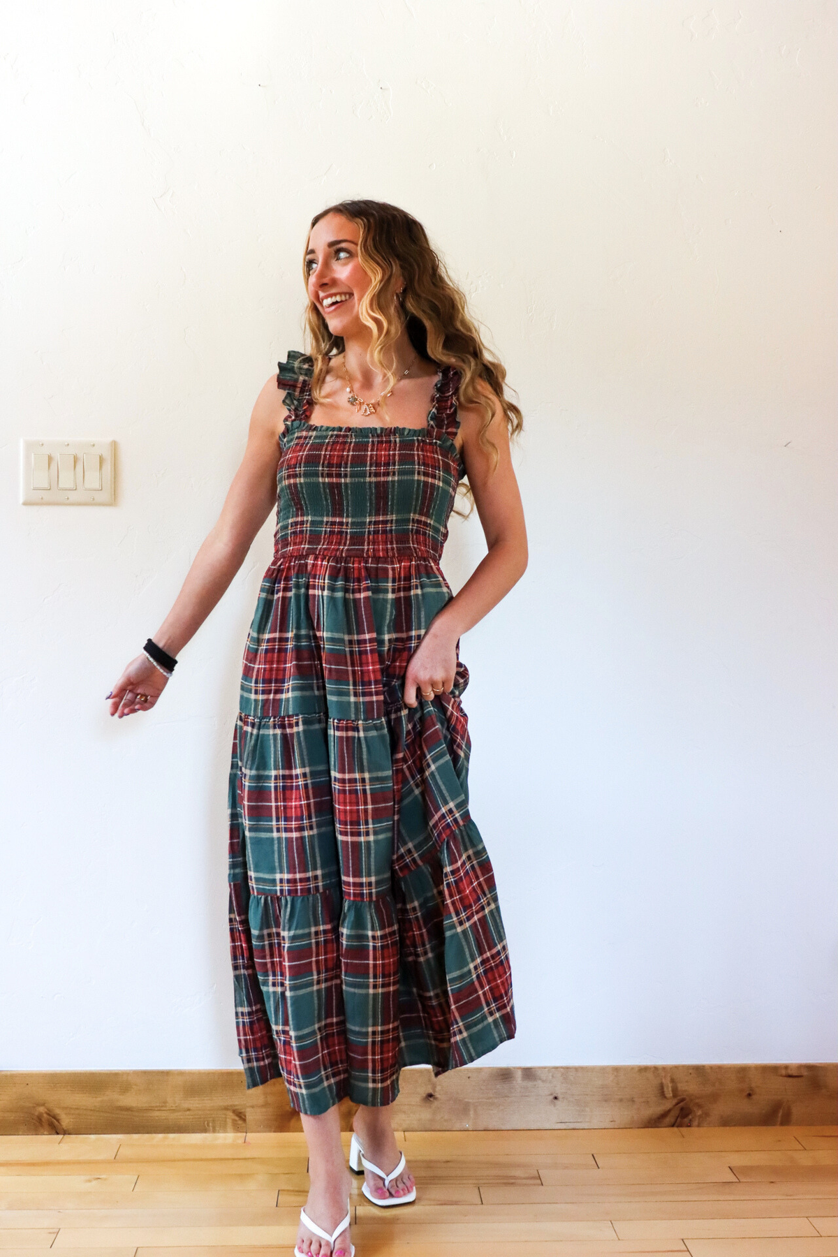 Woman wearing a plaid dress standing against a white wall.