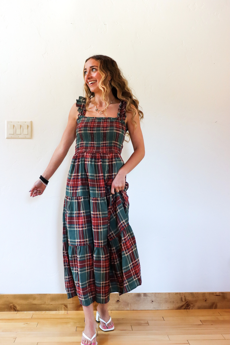 Woman wearing a plaid dress standing against a white wall.