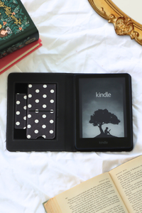 Kindle device in a black case with polka dot design on a white surface with books.