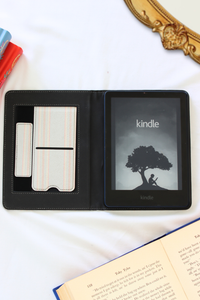 Kindle device in a black leather case on a white surface with books around