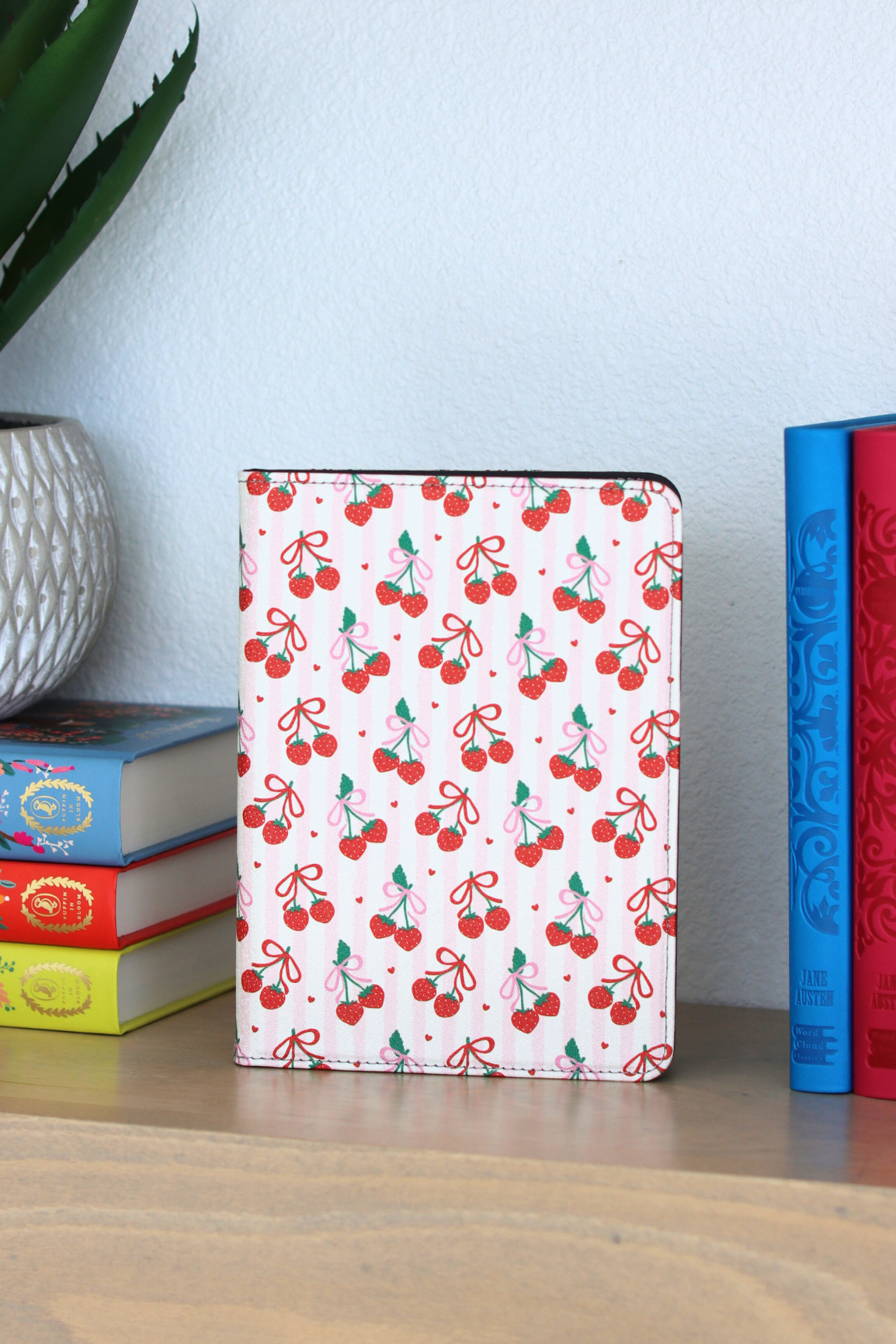 kindle with cherry pattern on a wooden surface with books and a plant in the background