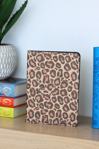 Leopard print kindle on a shelf with books and a plant in the background