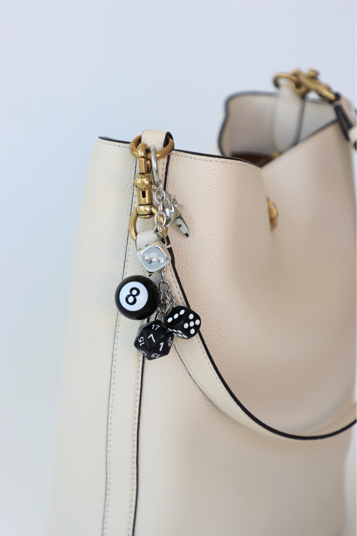 Beige handbag with decorative charm featuring a number 8 and dice on a light blue background