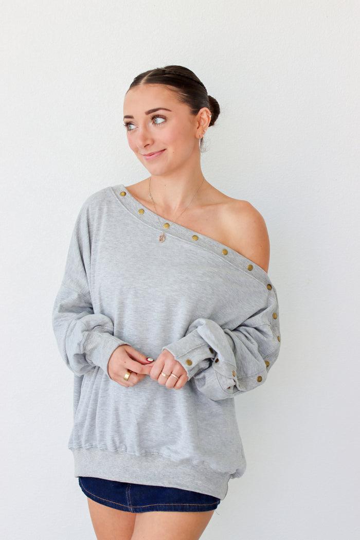 Woman wearing a light gray off the shoulder sweater with buttons along the trim 