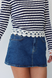 Person wearing a striped sweater and denim skirt on a white background