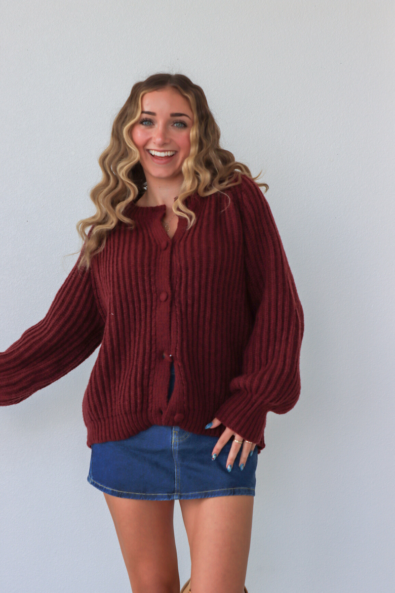 Woman wearing a maroon sweater and denim skirt against a white background