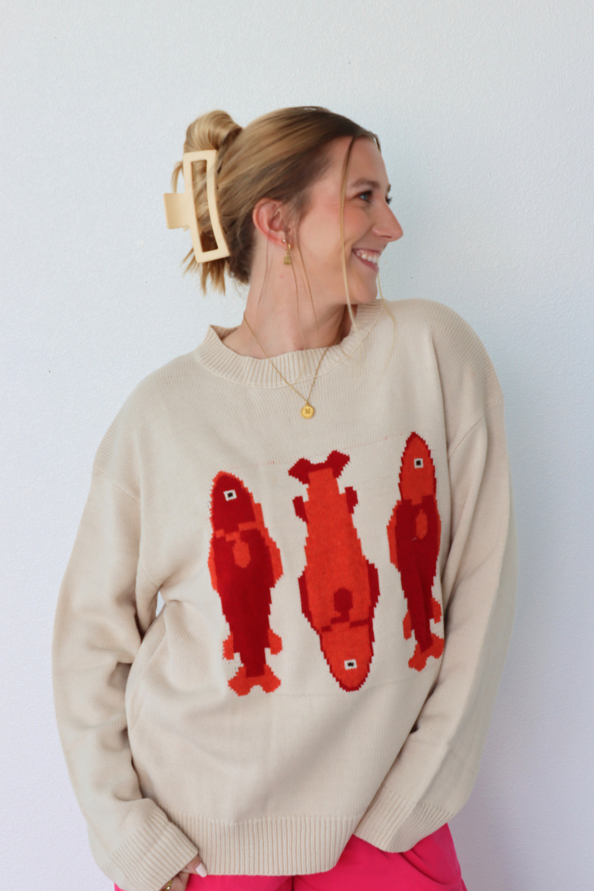 Woman wearing a beige sweater with red fish designs against a white background