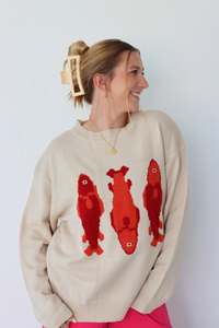 Woman wearing a beige sweater with red fish designs against a white background