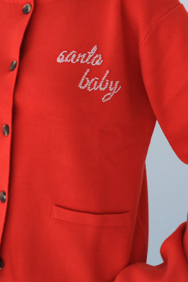 Red cardigan with 'Santa baby' embroidery on a light blue background