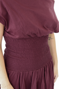 Close-up of a person wearing a dusty burgundy dress with a smocked elastic waist and a loose draped top.
