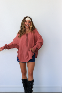 Woman wearing a pink blouse, blue shorts, and black boots against a white wall