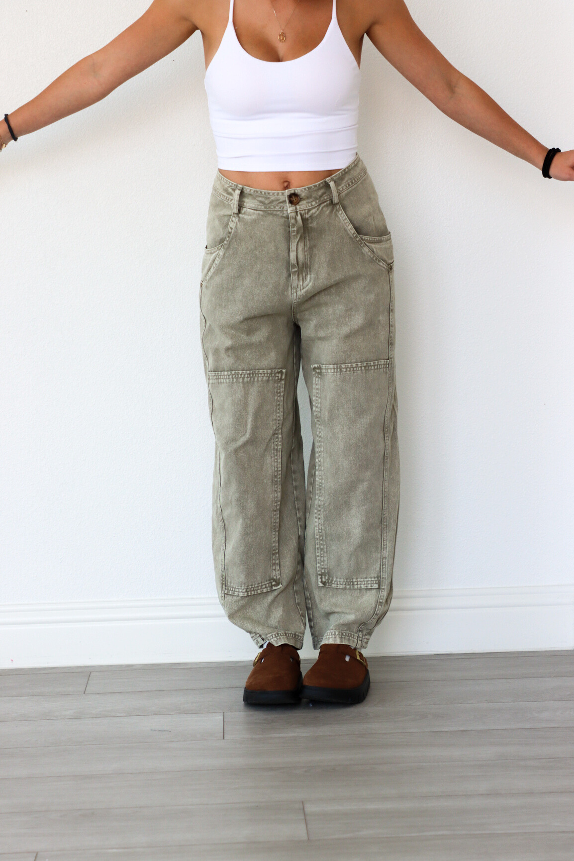 Person wearing a white tank top and olive green cargo pants against a white wall.