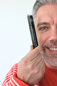 Man applying mascara with a black mascara tube labeled 'KVD' on a light gray background