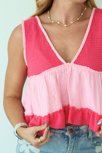 Woman wearing a pink and red layered top with denim shorts against a light blue background