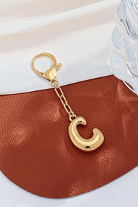 Gold crescent moon keychain on a brown leather surface with a white background