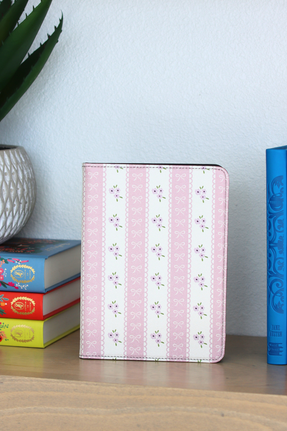 Pink floral striped kindle on a wooden surface with books and a plant in the background