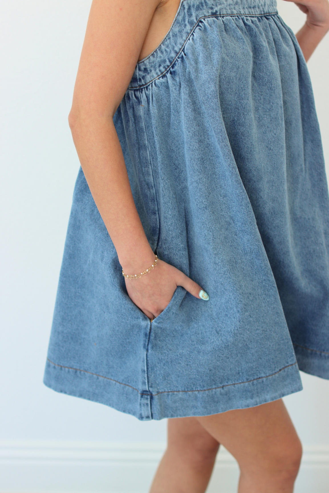 Woman wearing a denim blue mini dress with pockets against a white background
